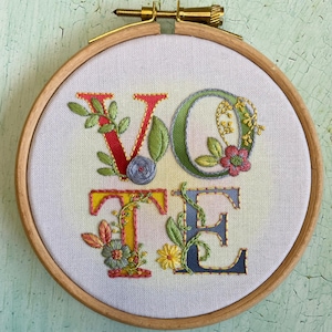 May include: Embroidered hoop art featuring the word "VOTE" in colorful letters with floral embellishments.