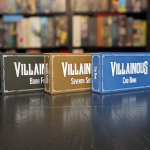 May include: Three game boxes, one green, one gold, and one blue, with the text "Villain" and "Villainous" on them. The boxes are for card games.