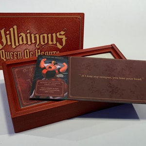 K&ouml;nnte beinhalten: Eine rote Box mit den Worten "Villainous Queen of Hearts" auf dem Deckel. Die Box ist ge&ouml;ffnet und enth&auml;lt eine Karte mit einem Bild der Herzk&ouml;nigin aus Disneys Alice im Wunderland. Die Karte lautet "Queen of Hearts -  BRUTAL TIFE" und "Zeige jedem Spieler eine Schurkenkarte. Sie m&uuml;ssen sofort einen Treffer einstecken."