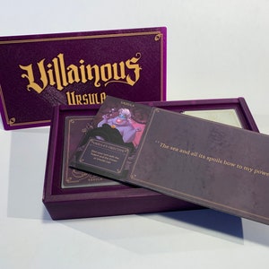 K&ouml;nnte beinhalten: Eine violette Box mit den Worten "Villainous Ursula" auf der Vorderseite. Die Box ist ge&ouml;ffnet und zeigt eine Karte mit einem Bild von Ursula aus Disneys Arielle, die Meerjungfrau. Die Karte lautet "Ursulas Ziel: Beginne deinen Zug mit dem Dreizack und der Krone in Ursulas Versteck". Die andere Karte lautet "Das Meer und all seine Sch&auml;tze beugen sich meiner Macht!"