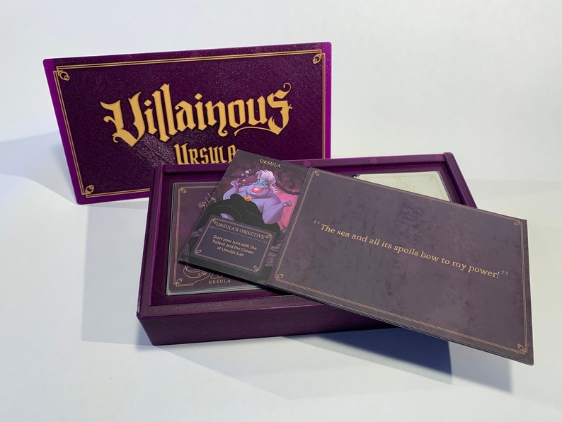 K&ouml;nnte beinhalten: Eine violette Box mit den Worten "Villainous Ursula" auf der Vorderseite. Die Box ist ge&ouml;ffnet und zeigt eine Karte mit einem Bild von Ursula aus Disneys Arielle, die Meerjungfrau. Die Karte lautet "Ursulas Ziel: Beginne deinen Zug mit dem Dreizack und der Krone in Ursulas Versteck". Die andere Karte lautet "Das Meer und all seine Sch&auml;tze beugen sich meiner Macht!"