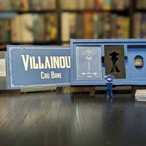May include: A blue box with a card game called "Villainous: Cad Bane" inside. The box has a black and white illustration of Cad Bane on the front. The game includes a blue plastic figure of Cad Bane.