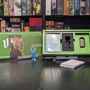 May include: A green game box with a card and a miniature figure. The card has a picture of a person with a crown and the text "Fire and chaos are one and I am the Lord of Chaos".