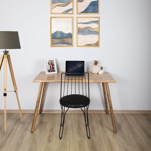 May include: A wooden desk with a black metal chair, a laptop, a framed photograph, and a potted plant. Four framed abstract landscape prints hang on the wall behind the desk.