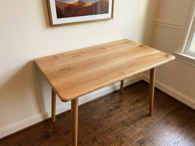 May include: A light-colored wooden desk with four rounded legs. The rectangular tabletop has rounded corners and a natural wood grain finish. The desk is approximately 48 inches long and 24 inches wide, suitable for a home office or study.