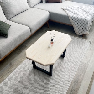 Könnte beinhalten: Ein heller Holz-Couchtisch mit rechteckiger Tischplatte und schwarzen Metallbeinen. Der Tisch steht auf einem hellgrauen Teppich.