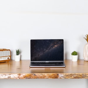 May include: A wooden desk with a laptop, a vintage radio, a camera, and decorative pineapple-shaped vases. Small potted plants are placed on the desk. The laptop screen displays a galaxy image.