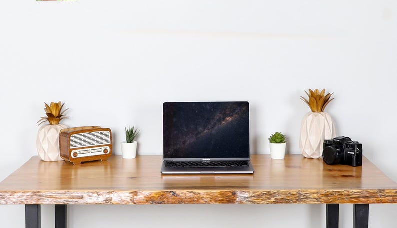 May include: A wooden desk with a laptop, a vintage radio, a camera, and decorative pineapple-shaped vases. Small potted plants are placed on the desk. The laptop screen displays a galaxy image.