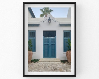 Peut inclure: Photographie encadrée d'un bâtiment blanc avec des portes et des volets bleu turquoise. Deux grands pots en terre cuite avec des plantes vertes encadrent l'entrée. Un chemin en pierre mène au bâtiment, et un palmier est visible au-dessus du toit.