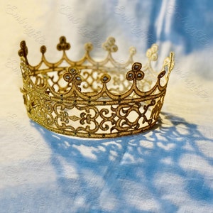 Può includere: Una corona dorata con un design delicato e intricato. La corona è realizzata in pizzo e ha una forma leggermente rialzata e arrotondata.