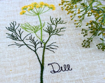 Può includere: Un quadrato di tessuto beige chiaro con il ricamo di una pianta di aneto con stelo verde e fiore giallo. La parola Dill è ricamata con filo viola scuro in corsivo sotto la pianta, che è centrata sul tessuto.