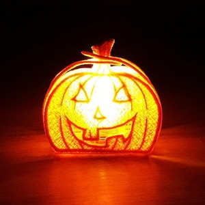 Pode incluir: Uma decoração de abóbora de Halloween laranja brilhante com um rosto esculpido. A abóbora tem olhos triangulares, uma boca em zigue-zague e um caule. O interior é iluminado, criando um brilho quente contra um fundo escuro.