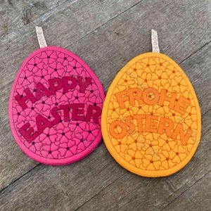 May include: Two felt Easter egg ornaments. One is pink with the text "Happy Easter" and the other is orange with the text "Frohe Ostern".