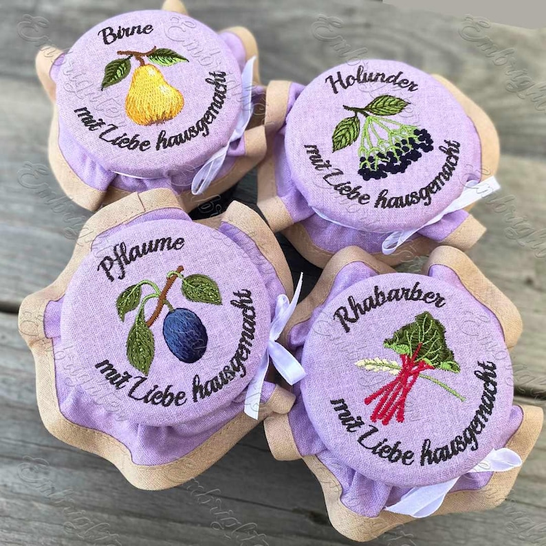 May include: Four purple fabric jars with embroidered lids. The lids have different fruit designs and the text "mit Liebe hausgemacht" which translates to "made with love homemade". The jars are labeled "Birne", "Pflaume", "Holunder", and "Rhabarber".