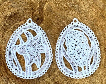 May include: Two white lace ornaments in the shape of an egg. One ornament features a floral design, while the other features a stylized flower.
