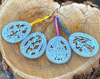 May include: Four blue lace Easter egg ornaments with floral designs, hanging from colorful ribbons on a wooden surface.