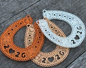 May include: Three horseshoe-shaped lace ornaments in shades of orange, tan, and white. Each horseshoe features the number "2026" and heart-shaped cutouts. The lace has a delicate, openwork design with decorative edges.