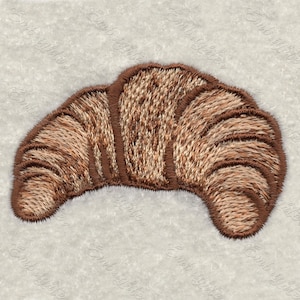 Könnte beinhalten: Ein braunes, gesticktes Croissant, ein klassisches französisches Gebäck, mit einem detaillierten Design.
