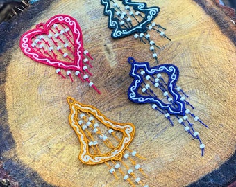 May include: Four embroidered Christmas ornaments in the shapes of a heart, a bell, and two Christmas trees. The ornaments are decorated with white beads and have a rustic, vintage look.