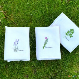 Pu&ograve; includere: Tre strofinacci da cucina bianchi con immagini ricamate di lavanda, erba cipollina e prezzemolo. Gli strofinacci hanno i nomi delle erbe scritti in tedesco sotto le immagini.