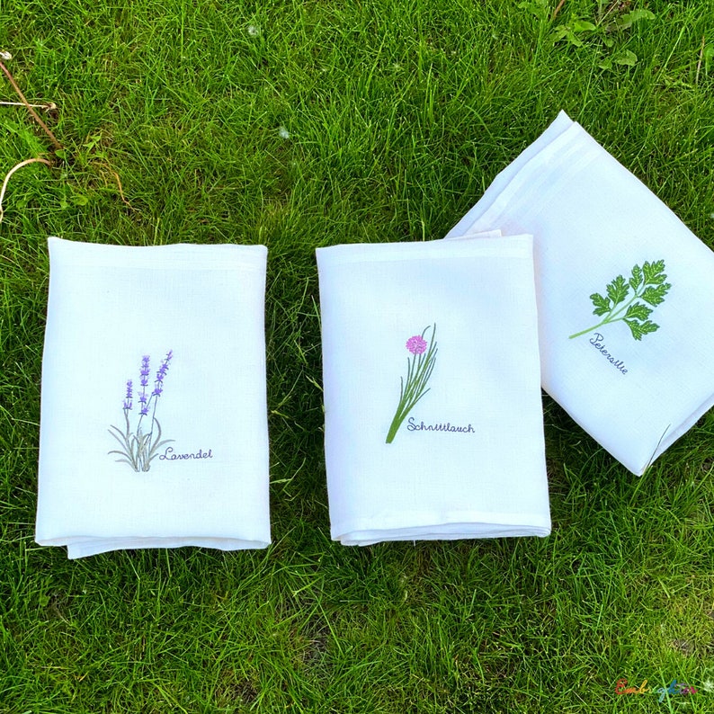 Pu&ograve; includere: Tre strofinacci da cucina bianchi con immagini ricamate di lavanda, erba cipollina e prezzemolo. Gli strofinacci hanno i nomi delle erbe scritti in tedesco sotto le immagini.