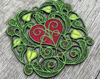 May include: Green and red embroidered heart design with intricate floral details. The heart is surrounded by a leafy vine pattern.