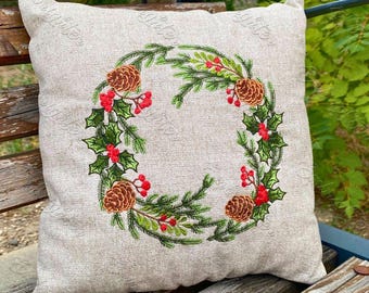 May include: A beige pillow with an embroidered Christmas wreath design. The wreath is made of green pine branches, red berries, and brown pine cones.