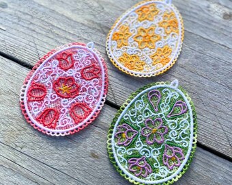 May include: Three embroidered Easter eggs with floral designs. The eggs are pink, yellow, and green with white accents.