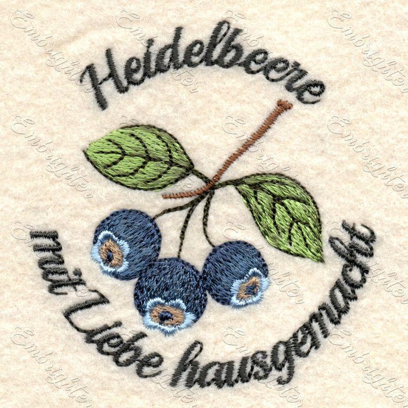 May include: Embroidered design featuring blueberries, green leaves, and text. The text reads "Heidelbeere mit Liebe hausgemacht" in a circular pattern around the blueberries. The blueberries are dark blue with light blue centers.