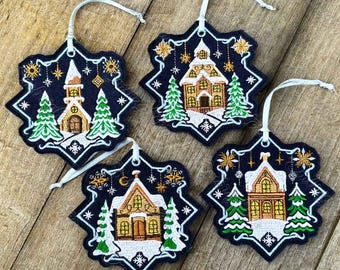 May include: Four snowflake-shaped Christmas ornaments with embroidered images of houses and trees. The ornaments are black with white and gold accents.