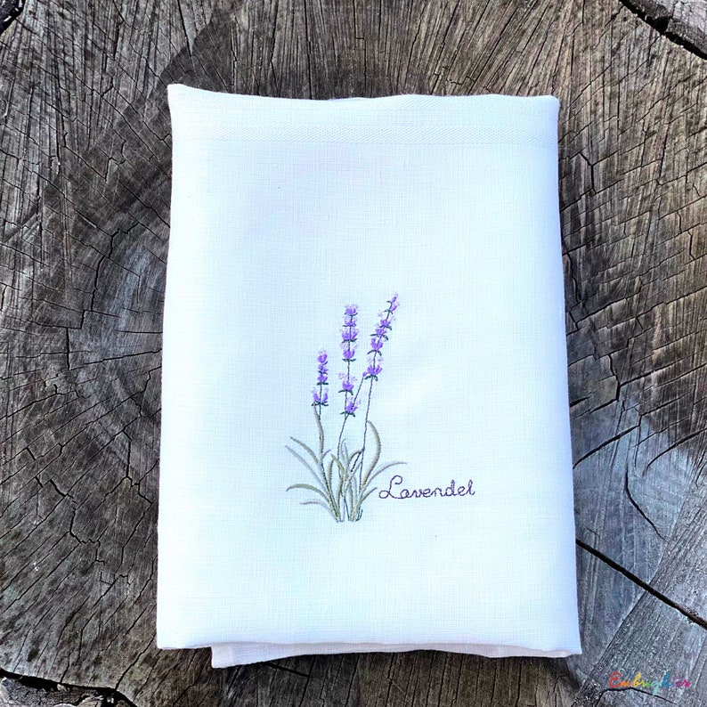 Pu&ograve; includere: Un asciugamano da t&egrave; in lino bianco con fiori di lavanda ricamati e la parola "Lavender" in corsivo.