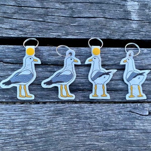 May include: Four gray and white seagull keychains with yellow accents. Each keychain features a different pose of the seagull.