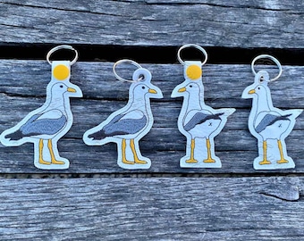 May include: Four gray and white seagull keychains with yellow accents. Each keychain features a different pose of the seagull.
