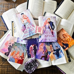May include: A flatlay of several fantasy romance novels with colorful covers. The books are titled "Once Upon a Broken Heart" and "The Ballad of Never After" by Stephanie Garber. The books are arranged on a wooden surface with a purple amethyst crystal.