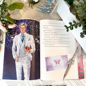 May include: A book open to a page with a blue and white illustration of a man holding a red apple. The text on the page reads "A Curse for True Love" and "Iridescent Fairytale".
