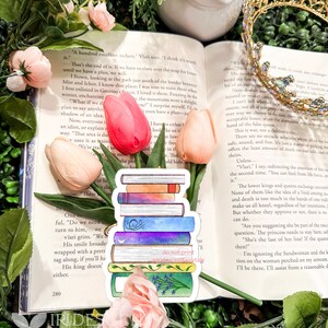 May include: A stack of colorful book stickers with a watercolor design, featuring a purple, blue, and green color scheme. The stickers are placed on an open book with pink and peach tulips and a gold crown in the background.
