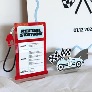 May include: A red and white Refuel Station sign with a list of drinks, a light blue race car with checkered flags, and a white background with a date. The sign has a red pump handle.