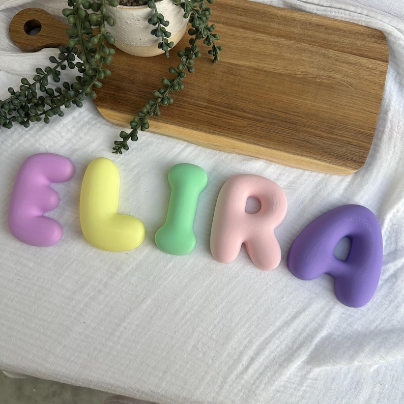 a wooden cutting board with the name "Elira" spelled out in colorful letters, along with a potted plant and a wooden board.