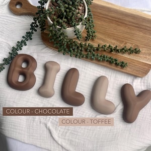 a collection of chocolate letters spelling out the name "Billy" arranged on a wooden surface.