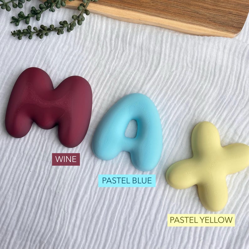 three pastel-colored letters on a white background, each labeled with a different color: maroon (WINE), pastel blue (PASTEAL BLUE), and pastel yellow (PASTEAL YELLOW).