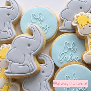 May include: Assortment of baby shower cookies. Elephant and giraffe-shaped cookies with light blue frosting circles that read "Oh Baby" in cursive. The cookies are decorated with light blue, yellow, and white icing.