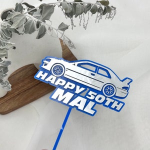 May include: A blue and silver car-shaped cake topper with the text "HAPPY 50TH MAL". The car has detailed wheels and a spoiler. The topper is on a blue stick, perfect for a birthday celebration.