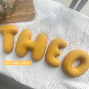 the letters "THEO" made of yellow dough or dough-like material, arranged on a white surface.
