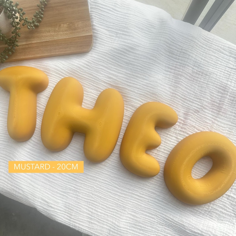 the letters "THEO" made of yellow dough or dough-like material, arranged on a white surface.