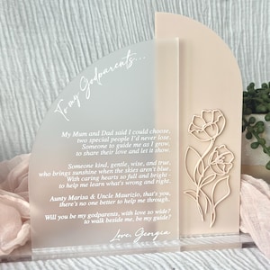 Può includere: Un ricordo in acrilico trasparente con una parte superiore ad arco rosa chiaro e un motivo floreale. Il testo "To my Godparents..." è in alto, con una poesia sotto. La base è trasparente e il design è elegante.