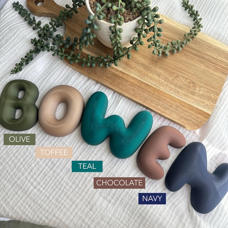 a collection of colorful letters arranged on a wooden board, with a potted plant and a wooden cutting board in the background.