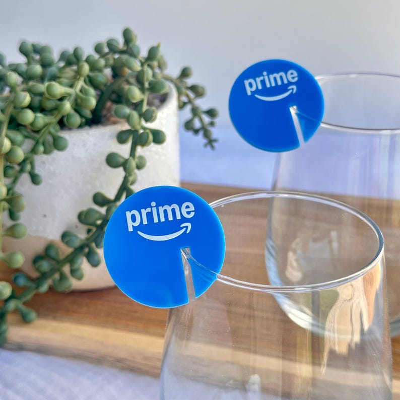 May include: Blue drink markers with the word "prime" and a curved arrow logo. The markers are placed on the rims of clear drinking glasses. A small potted plant is in the background.