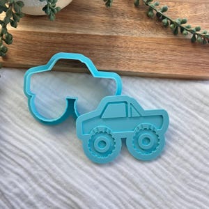 Könnte beinhalten: Zwei hellblaue Ausstechformen aus Kunststoff in Form von Monstertrucks. Eine Form zeigt die Umrisse der Karosserie, während die andere ein detailliertes Design mit großen, texturierten Rädern und einem Fensterrahmen des Führerhauses aufweist.