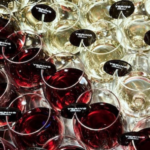 May include: An overhead shot of wine glasses filled with red and white wine. Each glass has a black label that reads "Yering Station". The glasses are arranged closely together, creating a visually appealing display.