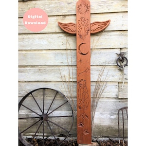 May include: A wooden totem pole with carvings of a sun, a bird with wings spread, a crescent moon, a star, a constellation, a bear, mountains, and bear paw prints.